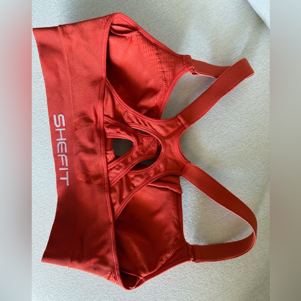 Two SHEFIT Racerback Sports Bras. One red; one tan.